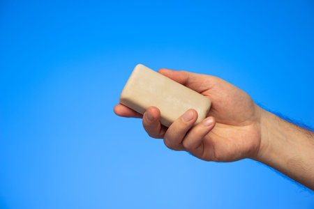Bar of soap held in hand by Caucasian isolated on blue background studio shot.