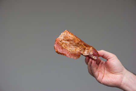 Raw seasoned sliced pork rib held by Caucasian male hand studio shot isolated on gray background.の写真素材