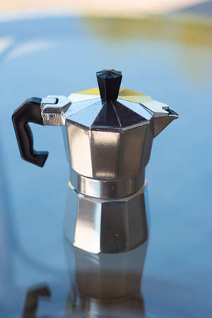 Classic metal moka pot coffee maker on a glass table with reflection shallow depth of field.の写真素材