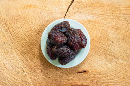 Big pitted dried dates on a small white plate set on a wooden boar top view.
