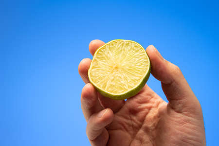 Fresh green halved lime held in hand by Caucasian male hand close up shot isolated on blue background.の写真素材