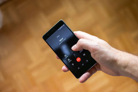 Caucasian male hand dialing his Mom on his cell phone. Close up shot, shallow depth of field, brown interior defocused background.の写真素材