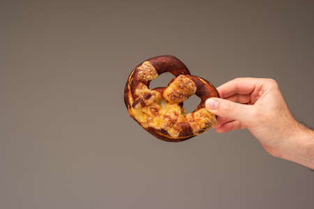 Freshly home backed Pretzel held in hand by Caucasian male hand. Close up studio shot, isolated on gray.の写真素材