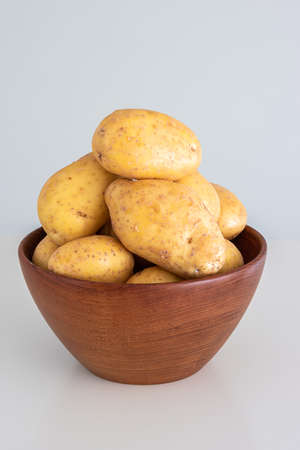 Group of fresh raw potatoes in a wooden bowl. Close up studio shot, no people.の写真素材