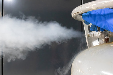 Operator hand in blue protective glove releasing the pressure valve on a liquid nitrogen tank. Close up shot.の写真素材