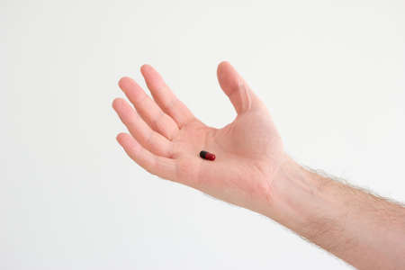 Caucasian male hand holding a medical black and red capsule pill in his palm.の写真素材