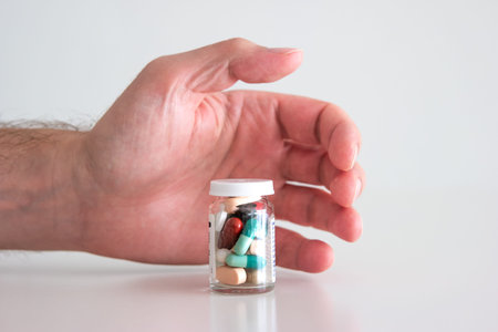 Caucasian male hand reaching out for a glass bottle full of various colored medical pillsの写真素材