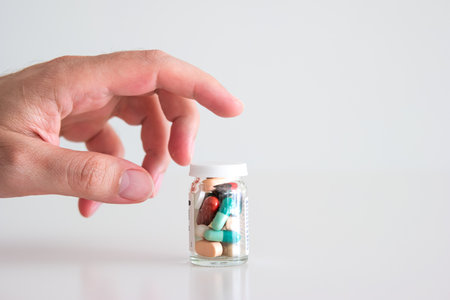 Caucasian male hand reaching out for a glass bottle full of various colored medical pillsの写真素材