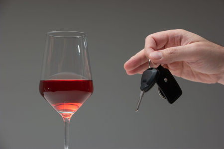 Drinking and driving concept shot. Male hand holding car keys next to tall wine glass, studio shot.