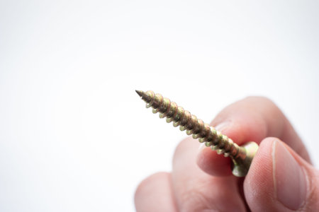 Small metal threaded screw held by Caucasian male hand between fingers. Close up studio macro shot,...