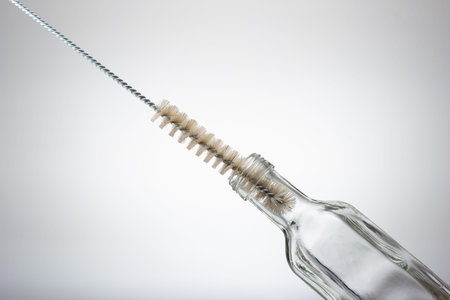 Thin wire brush for cleaning bottles. Inside small empty glass bottle. Close up studio shot,...