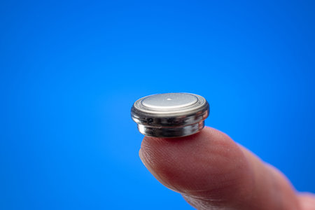 Caucasian male hand holding a button type battery between fingers. Close up studio shot, isolated on...