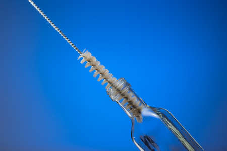 Thin wire brush for cleaning bottles. Inside small empty glass bottle. Close up studio shot, isolated on blue background.の写真素材
