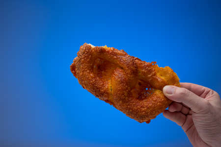 Half of Pretzel held by male hand. Close up studio shot, isolated on blue background.の写真素材