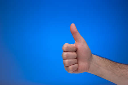Thumb's up like gesture made by Caucasian male hand. Close up studio shot, isolated on blue background.の写真素材