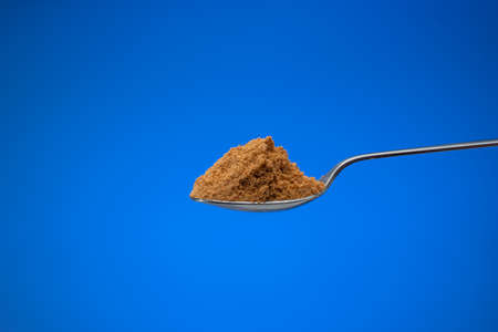 Finely ground meat seasoning powder in a small silver spoon. Close up studio shot, isolated on blue background.の写真素材