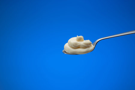 Fresh homemade mayonnaise in a small spoon. Close up studio shot, isolated on blue background.の写真素材