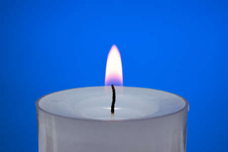 Single small white candle burning. Close up studio shot, isolated on blue background.の写真素材