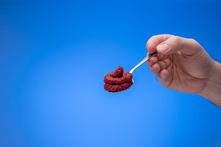 Red tomato concentrate paste in a small spoon held in male hand. Close up studio shot, isolated on...