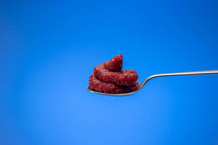 Red tomato concentrate paste in a small spoon. Close up studio shot, isolated on blue background.の写真素材