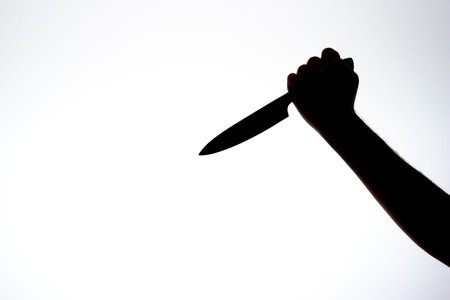 Silhouette on a male arm holding a long kitchen knife threateningly. Close up studio shot, isolated...