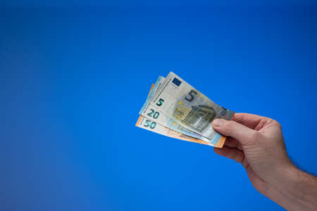 Euro currency banknotes held by male hand. Close up studio shot, isolated on blue background.の写真素材