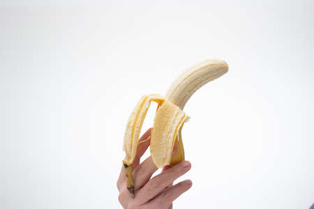 Ripe yellow half peeled banana held in hand by Caucasian male hand. Close up studio shot, isolated on white background.の写真素材