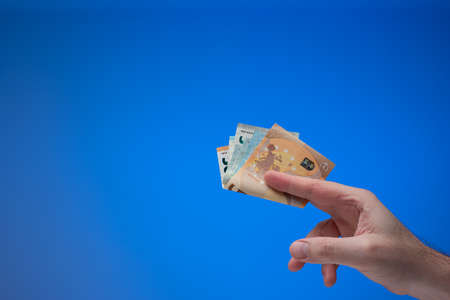 Euro currency banknotes held by male hand. Close up studio shot, isolated on blue background.の写真素材