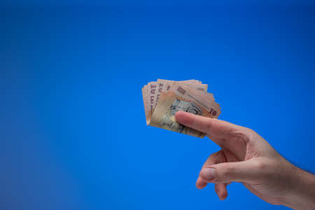 Romanian Lei currency banknotes held by male hand. Close up studio shot, isolated on blue background.の写真素材