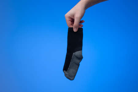 Single dry and clean cotton sock held in hand by Caucasian male hand. Close up studio shot, isolated on blue background.の写真素材