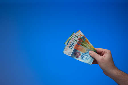 Swiss franc banknotes held by male hand. Close up studio shot, isolated on blue background.の写真素材