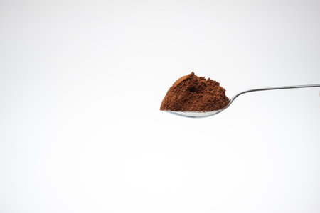 Fresh ground coffee powder on a metal spoon. Close up studio shot, isolated on white background.の写真素材