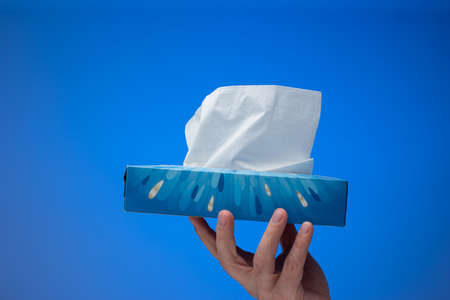 Paper tissue dispenser held by Caucasian male hand. Close up studio shot, isolated on blue background.の写真素材