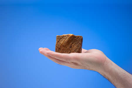 Old style homemade artisanal soap bar held in male palm. Close up studio shot, isolated on blue background.の写真素材