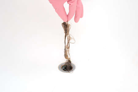 Clump of wet hair being removed from a bathtub sinkhole by male hand in pink latex glove. Close up shot, front view.の写真素材