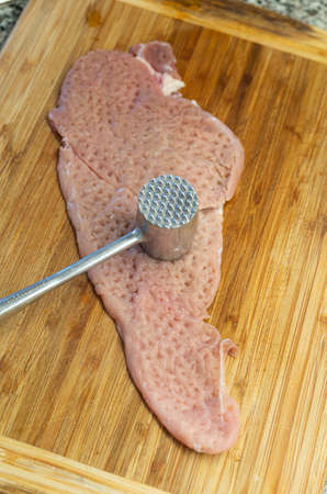 Beater raw piece of Schnitzel meat and a metal meat tenderizer mullet. Close up shot, top view, shallow depth of field, no people.の写真素材