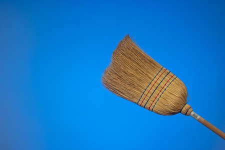 Straw broom with wooden handle. Close up studio shot, isolated on blue background.の写真素材