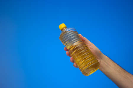 Rapeseed or sunflower cooking oil held by Caucasian male hand. Close up studio shot, isolated on blue background.の写真素材
