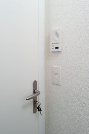 Thick and sturdy white apartment door with keys in the door lock. Inside view, no people. Intercom...