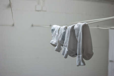 White pajamas or clothing and short socks hanging from drying lines inside communal laundry room inside apartment building. No people.の写真素材
