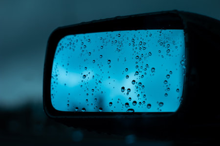 Car side mirror with rain water droplets. Cloudy dark weather, shallow depth of field. Close up shot, no people.の写真素材