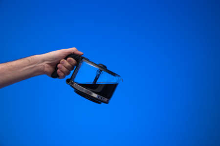 Homemade large glass coffee pot held in hand by man making a pouring gesture. Close up studio shot, isolated on blue background.の写真素材