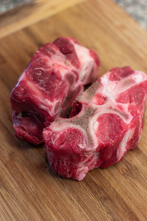 Fresh raw veal or beef leg or neck bones with meat. Soup and stock ingredients, close up shot on wooden kitchen board, no people.の写真素材