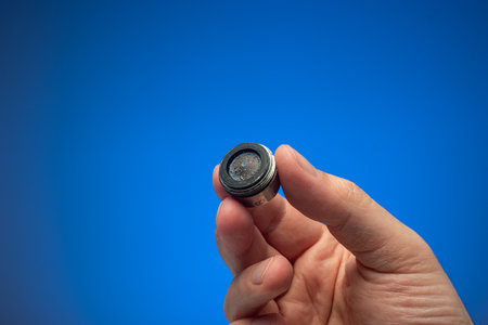 Old dirty limescale covered clogged up tap water faucet strainer or aerator held in hand by Caucasian male. Close up studio shot, isolated on blue background.の写真素材