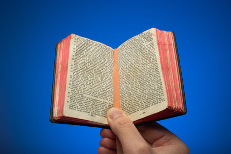 Old vintage small opened Bible book held in hand by Caucasian male. Close up studio shot, isolated...