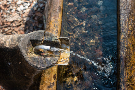 Old rustic drinking water fountain in the forest. Wooden construction, rusty metal pipe and faucet,...
