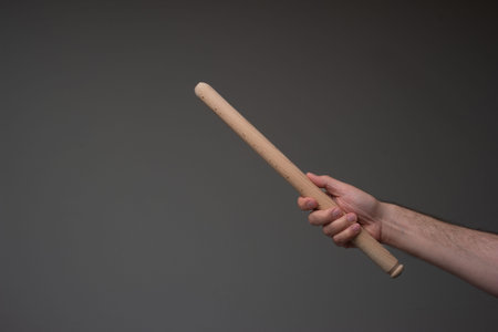 Wooden kitchen rolling pin held in hand by Caucasian male. Close up studio shot, isolated on gray...