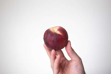 Fresh ripe peach held in hand by Caucasian male hand. Close up studio shot, isolated on a white background.の写真素材