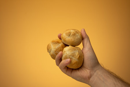 Homemade oven backed small panini bun held in hand by Caucasian male hand. Close up studio shot, isolated on orange background.の写真素材