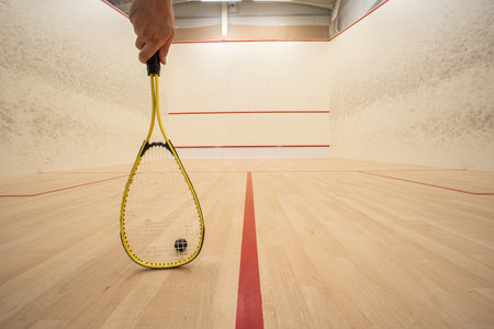 Male hand holding a racket inside a squash court. Low angle, unrecognizable person, large depth of fieldの写真素材